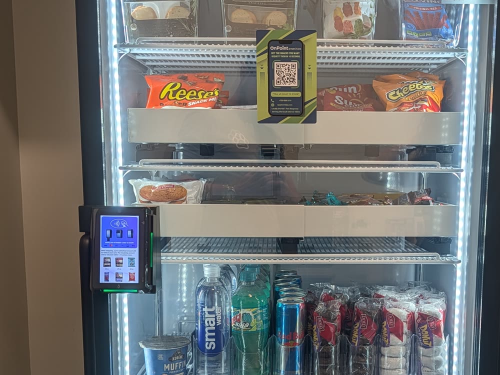 Close view of an On Point smart cooler: lit shelves, request-line QR card, cashless reader