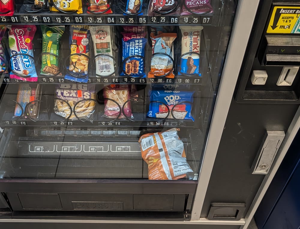 An old snack vending machine with a bag stuck sideways in the delivery tray