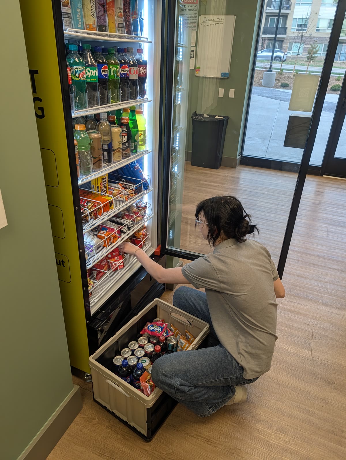 A member of the On Point Amenities family crouched at a smart cooler, restocking it from a supply crate